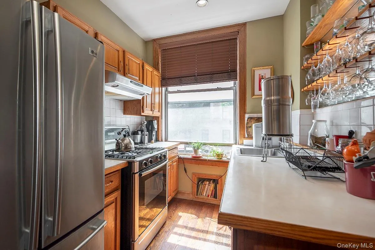 Kitchen with appliances with stainless steel finishes, light countertops, under cabinet range hood, light wood-style flooring, and brown cabinetry Kitchen with appliances with stainless steel finishes, light countertops, under cabinet range hood, light wood-style flooring, and brown cabinetry