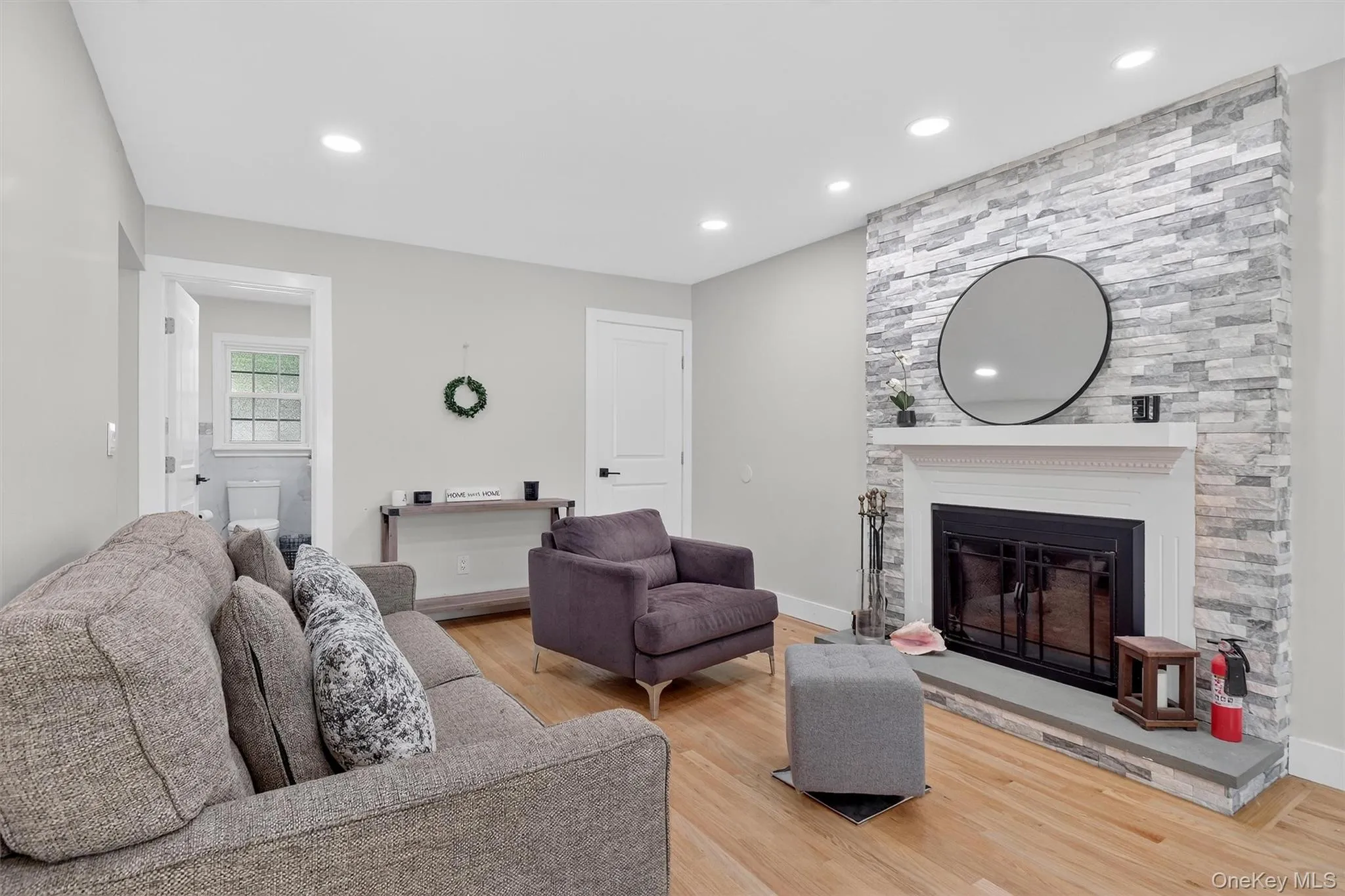 Living room featuring light wood-style floors, a large fireplace, and recessed lighting Living room featuring light wood-style floors, a large fireplace, and recessed lighting