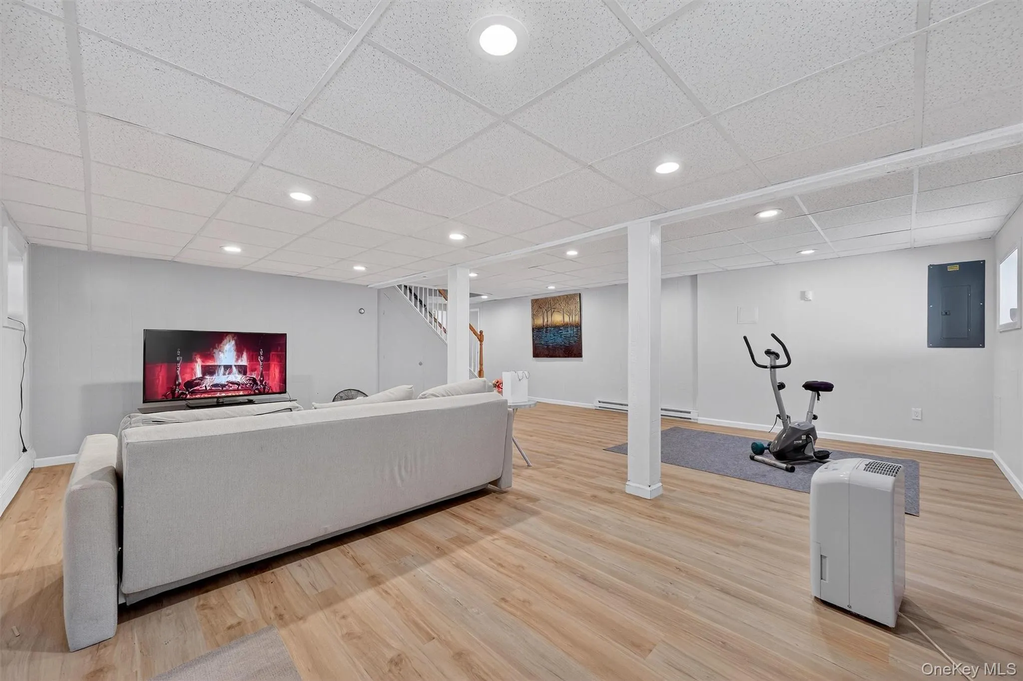 Lower Level - Living area featuring electric panel, stairway, light wood-style flooring, recessed lighting, and a paneled ceiling Lower Level - Living area featuring electric panel, stairway, light wood-style flooring, recessed lighting, and a paneled ceiling