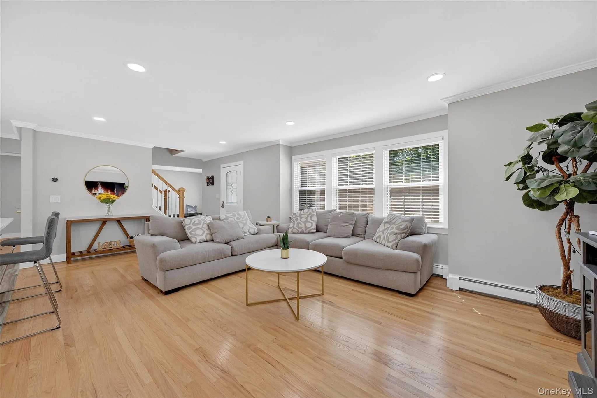 Living area with crown molding, light wood-type flooring, stairway, baseboard heating, and recessed lighting Living area with crown molding, light wood-type flooring, stairway, baseboard heating, and recessed lighting