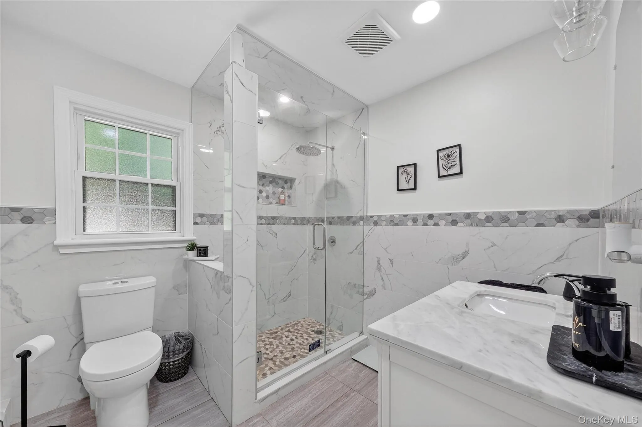 Bathroom featuring tile walls, wainscoting, vanity, and a marble finish shower Bathroom featuring tile walls, wainscoting, vanity, and a marble finish shower