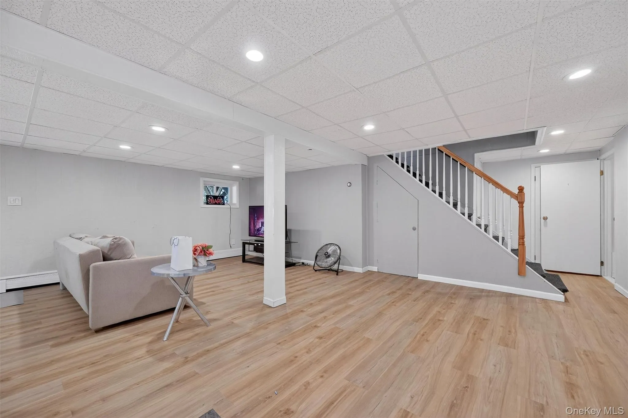 Lower Level - Living area with recessed lighting, light wood-style flooring, stairs, a drop ceiling, and baseboard heating Lower Level - Living area with recessed lighting, light wood-style flooring, stairs, a drop ceiling, and baseboard heating