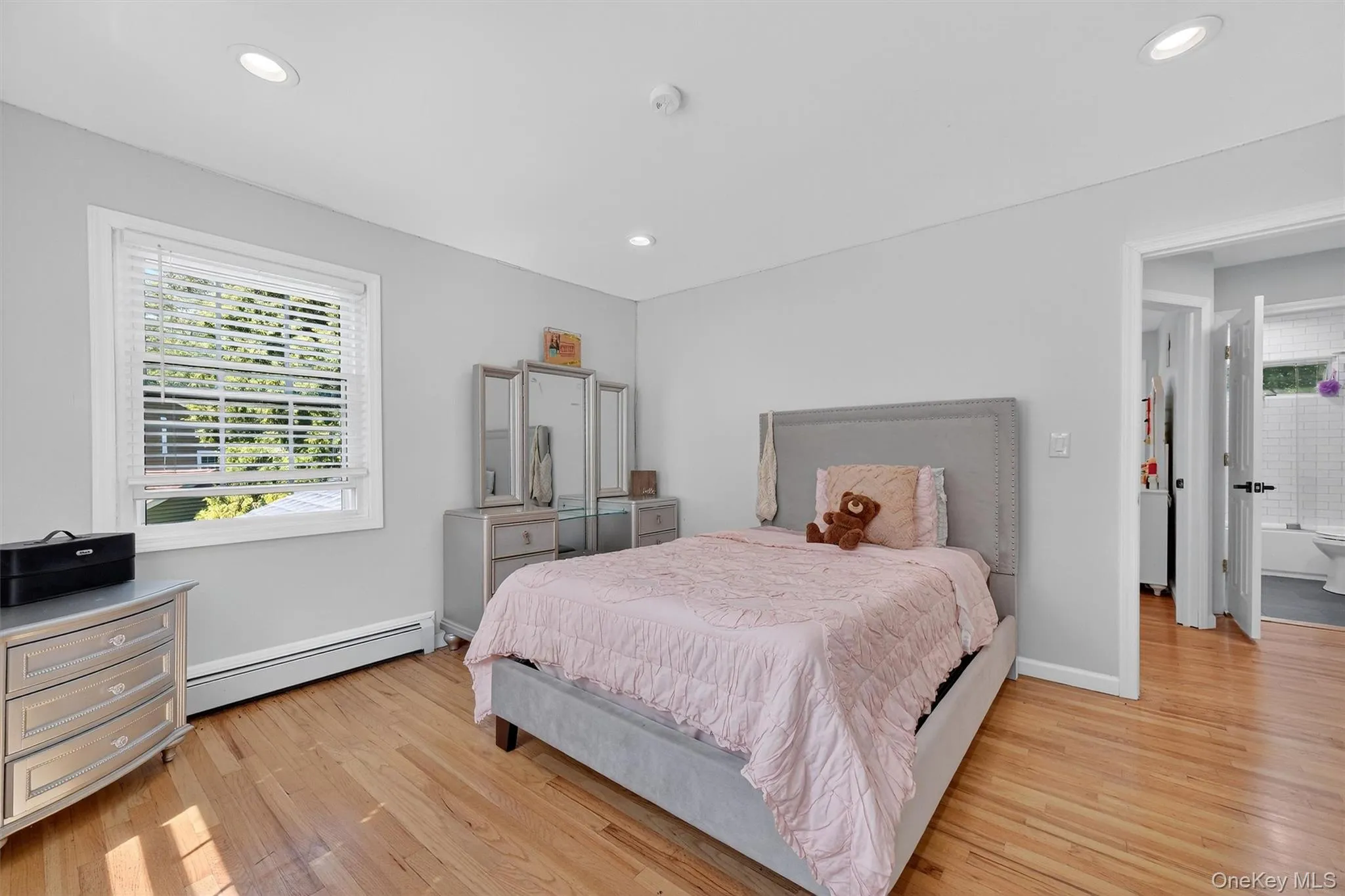 Bedroom with a baseboard heating unit, light wood finished floors, and recessed lighting Bedroom with a baseboard heating unit, light wood finished floors, and recessed lighting