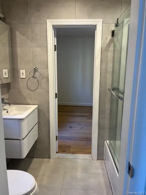Full bath with tile walls, shower / bath combination with glass door, vanity, and light tile patterned floors Full bath with tile walls, shower / bath combination with glass door, vanity, and light tile patterned floors