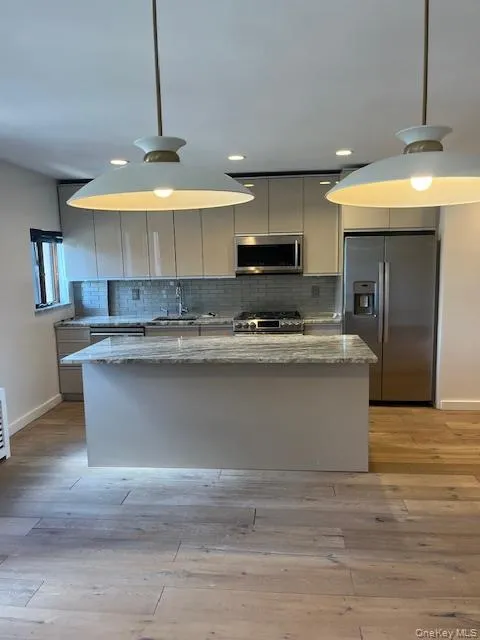 Kitchen featuring appliances with stainless steel finishes, light stone counters, tasteful backsplash, and light wood-type flooring Kitchen featuring appliances with stainless steel finishes, light stone counters, tasteful backsplash, and light wood-type flooring