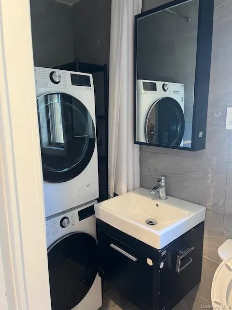 Half bath featuring vanity, tile walls, and stacked washer / drying machine Half bath featuring vanity, tile walls, and stacked washer / drying machine