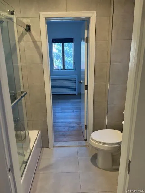 Bathroom with tile walls, combined bath / shower with glass door, and light tile patterned floors Bathroom with tile walls, combined bath / shower with glass door, and light tile patterned floors