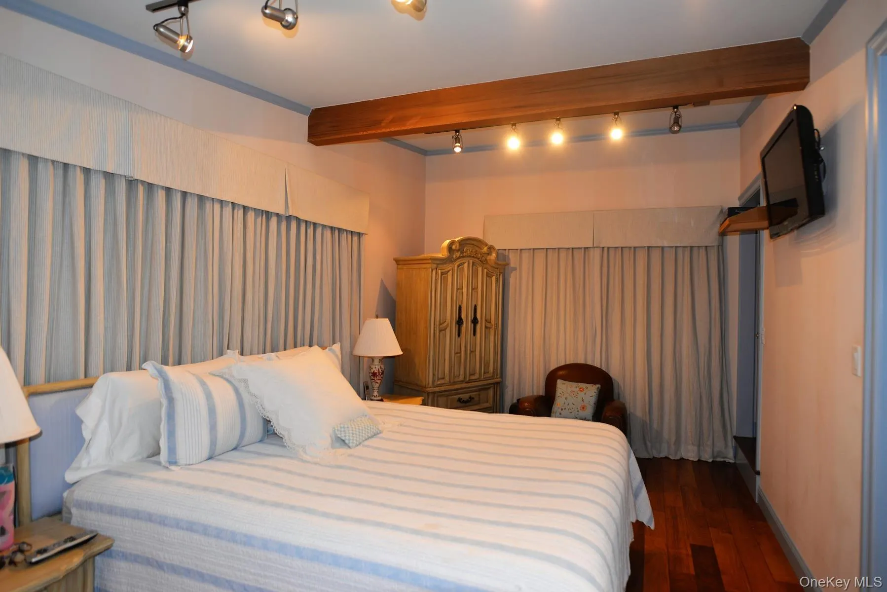 Bedroom with dark wood-style flooring, rail lighting, and beamed ceiling