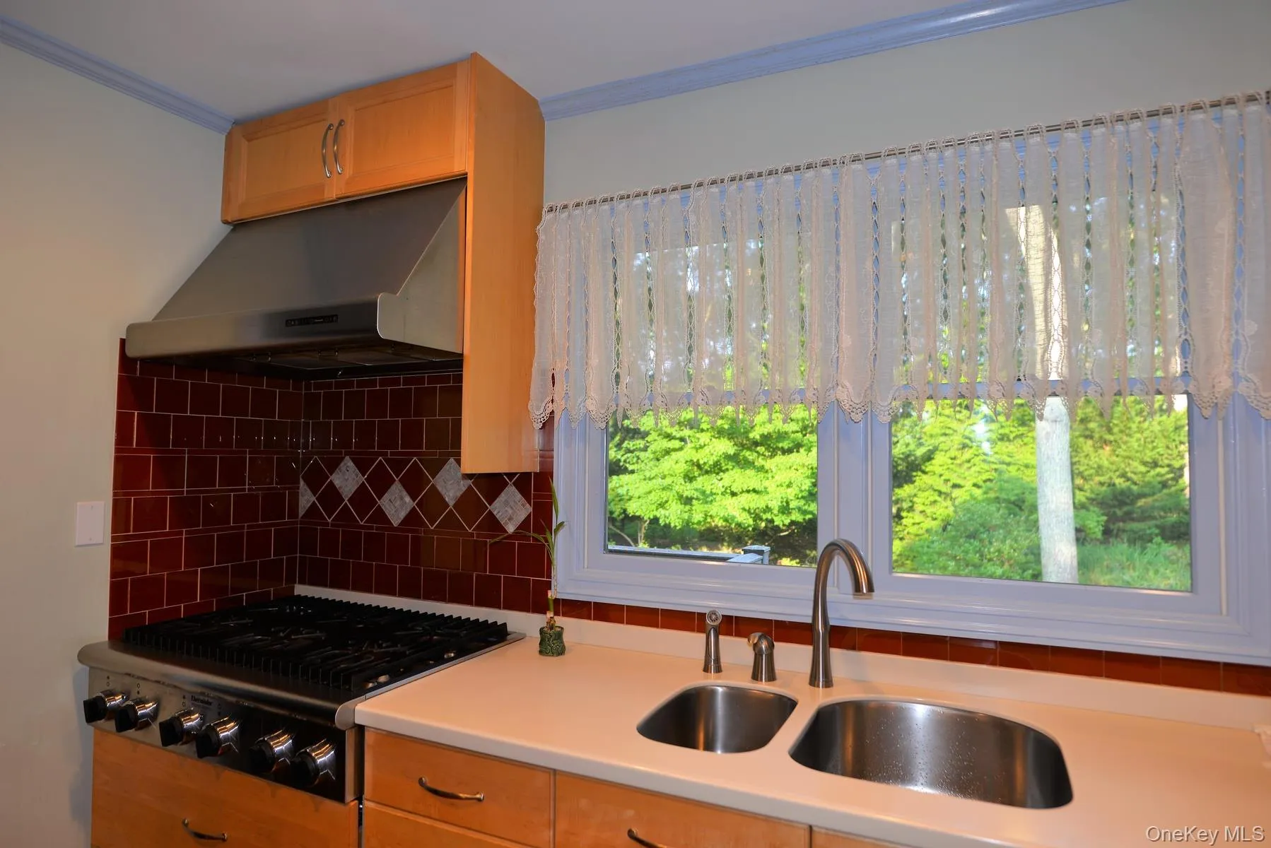 Kitchen with decorative backsplash, under cabinet range hood, light countertops, crown molding, and gas stovetop