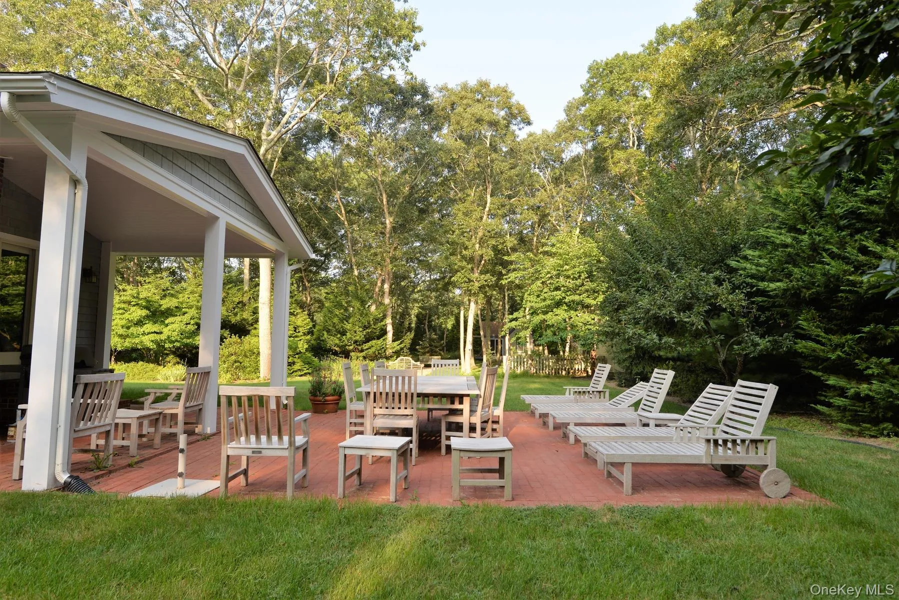 View of grassy yard featuring view of wooded area, a wooden deck, and a patio