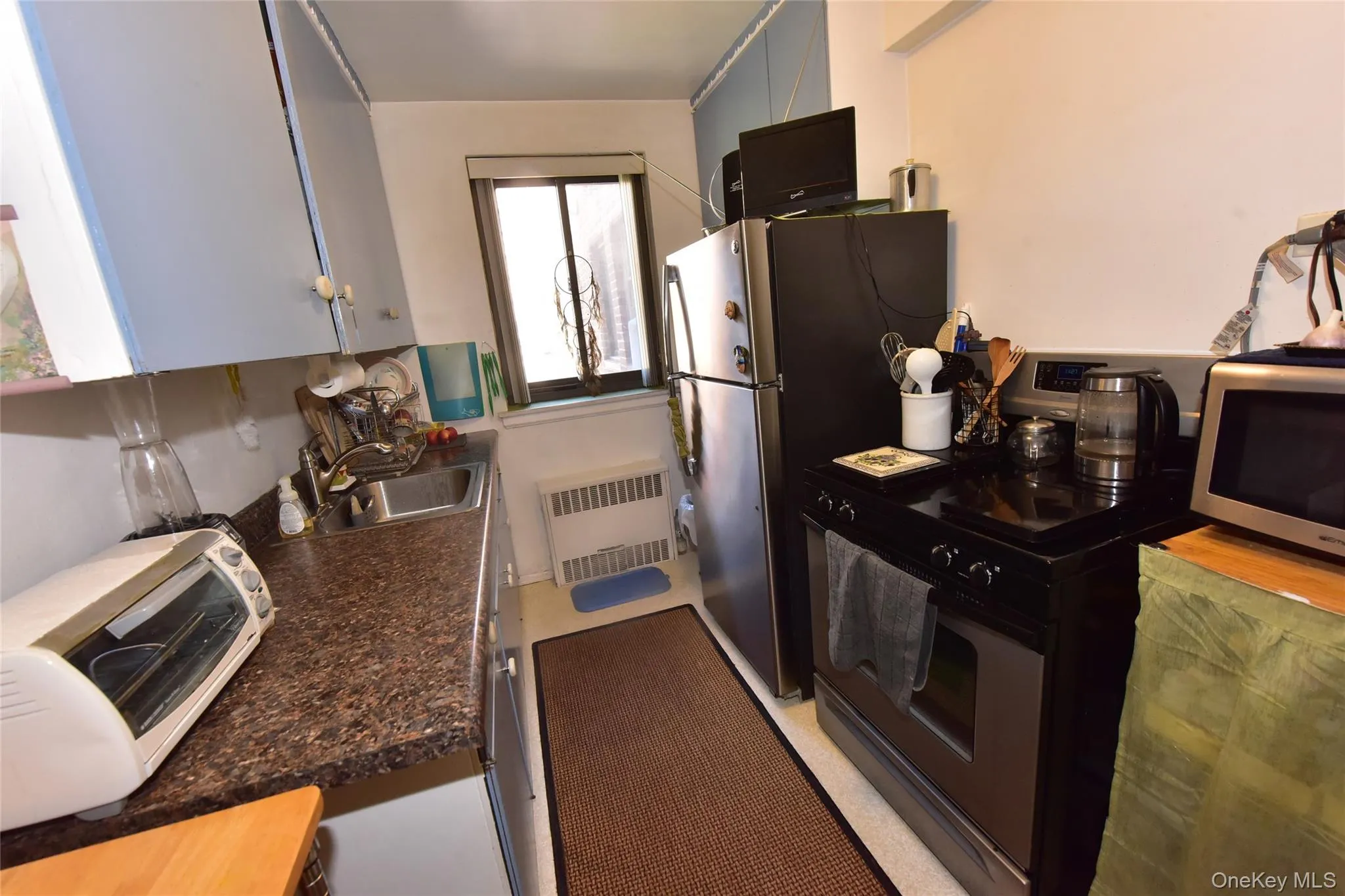 Kitchen with black range with gas cooktop, radiator heating unit, dark countertops, and stainless steel microwave Kitchen with black range with gas cooktop, radiator heating unit, dark countertops, and stainless steel microwave