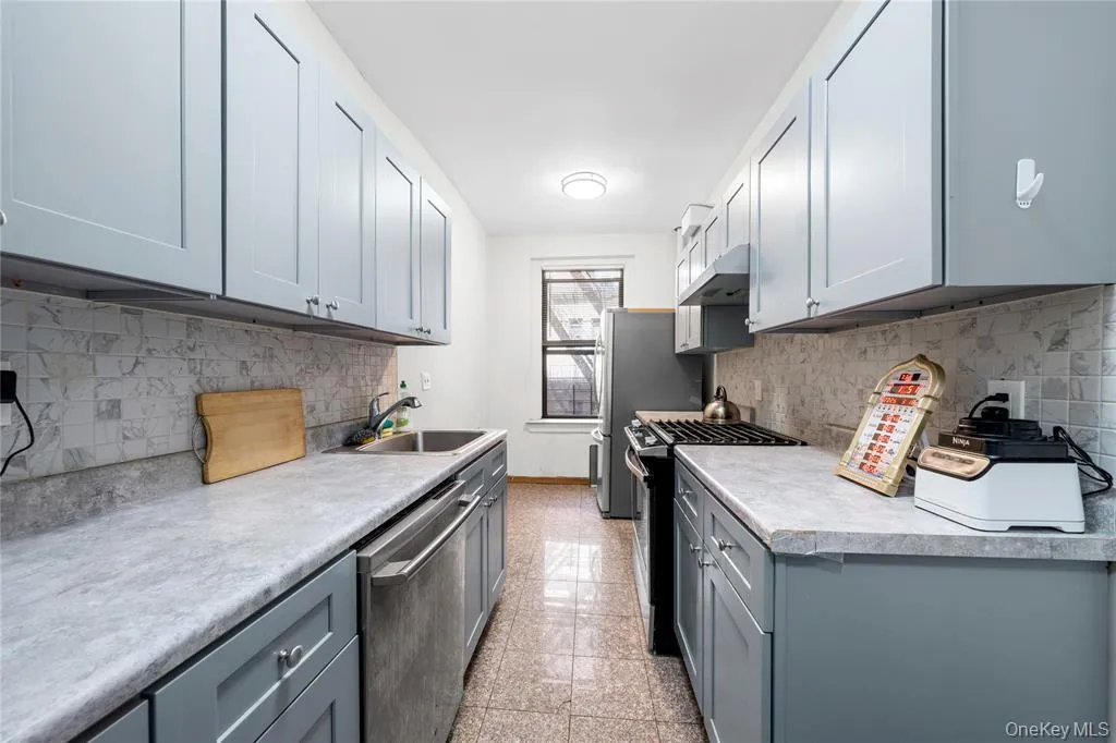 Kitchen featuring gray cabinets, gas range oven, backsplash, stainless steel dishwasher, and light countertops Kitchen featuring gray cabinets, gas range oven, backsplash, stainless steel dishwasher, and light countertops