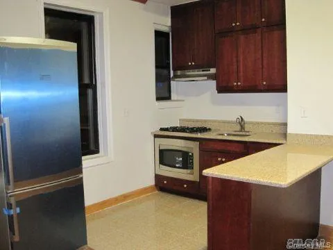 Kitchen with freestanding refrigerator, under cabinet range hood, a peninsula, and light stone countertops Kitchen with freestanding refrigerator, under cabinet range hood, a peninsula, and light stone countertops