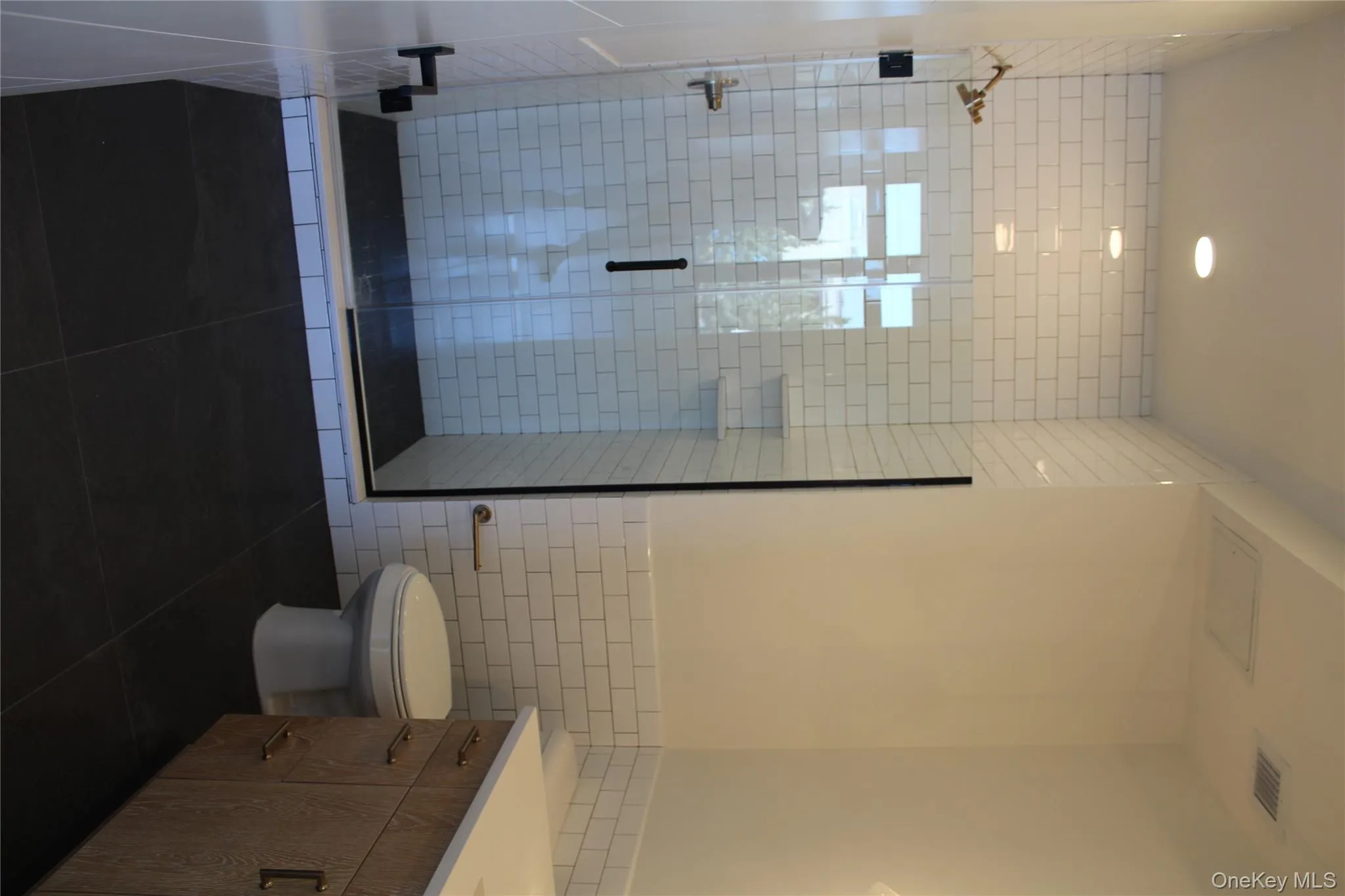 Full bath featuring tile walls, dark tile patterned floors, vanity, a shower stall, and wainscoting Full bath featuring tile walls, dark tile patterned floors, vanity, a shower stall, and wainscoting