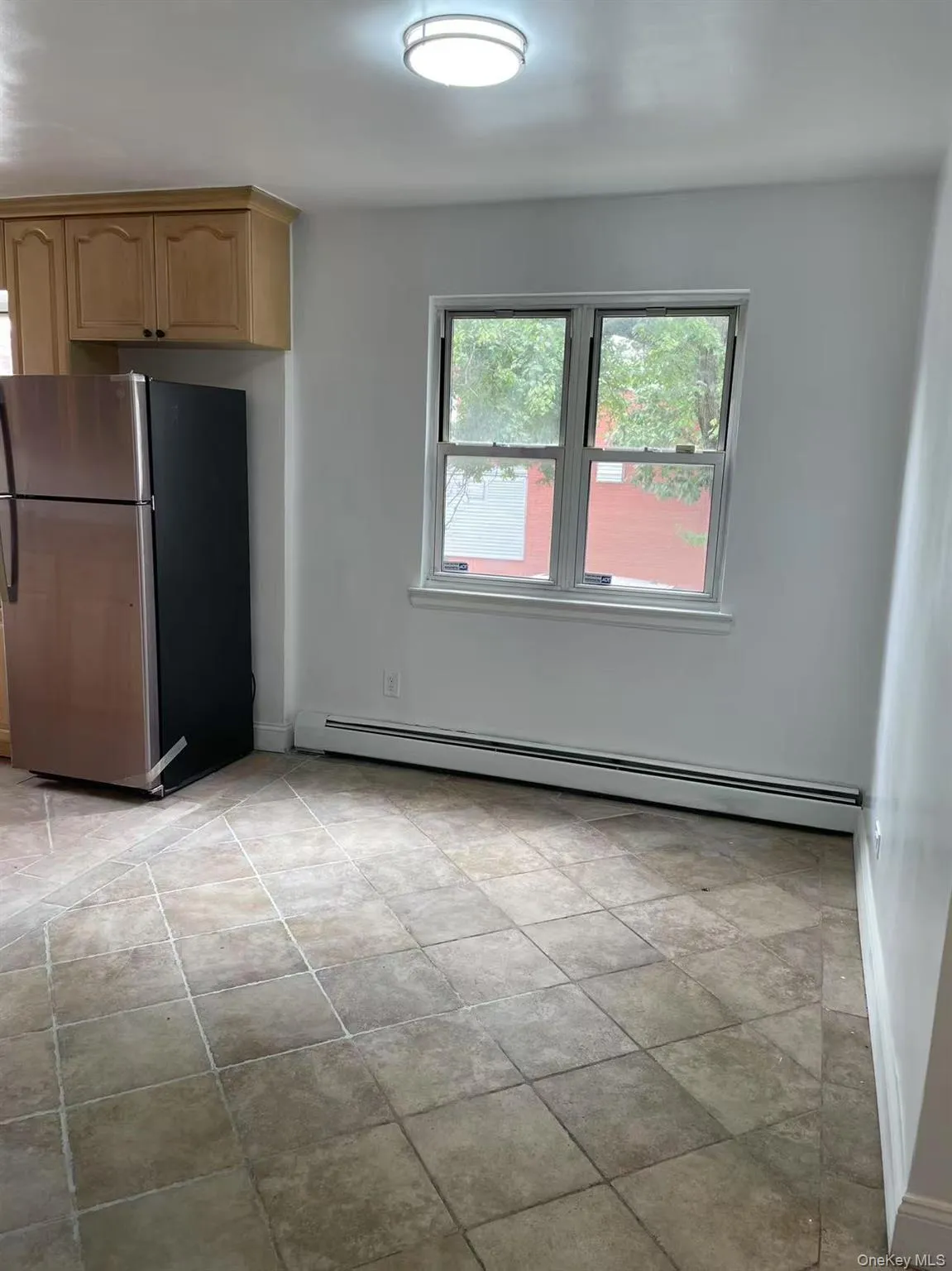 Kitchen with freestanding refrigerator, a baseboard radiator, and light brown cabinets Kitchen with freestanding refrigerator, a baseboard radiator, and light brown cabinets
