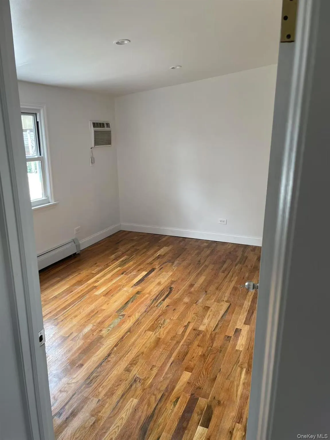 Spare room with light wood-style floors, baseboard heating, and a wall mounted AC Spare room with light wood-style floors, baseboard heating, and a wall mounted AC