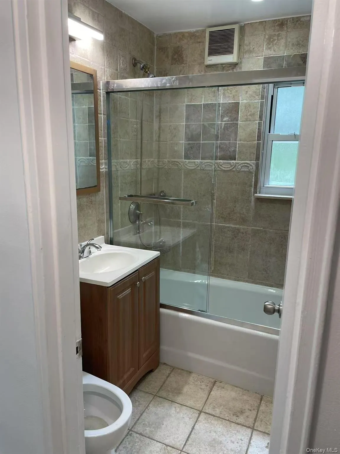 Bathroom with shower / bath combination with glass door, vanity, and light tile patterned floors Bathroom with shower / bath combination with glass door, vanity, and light tile patterned floors