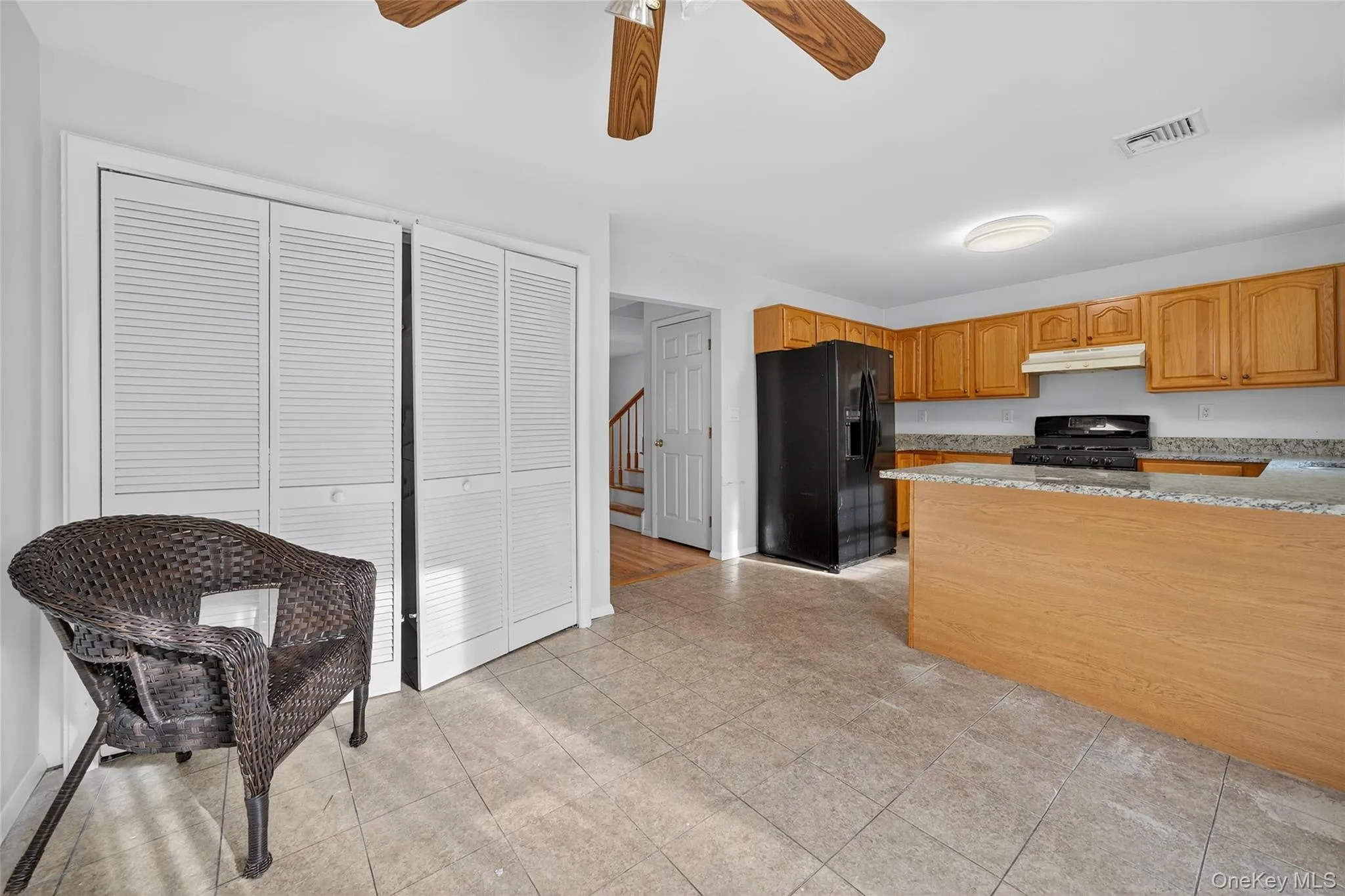 Kitchen with light stone counters, black appliances, a ceiling fan, under cabinet range hood, and brown cabinetry Kitchen with light stone counters, black appliances, a ceiling fan, under cabinet range hood, and brown cabinetry