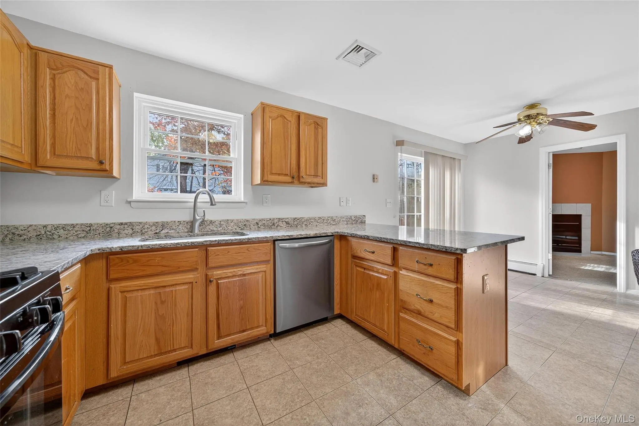 Kitchen featuring black gas range, dishwasher, light stone countertops, a peninsula, and brown cabinetry Kitchen featuring black gas range, dishwasher, light stone countertops, a peninsula, and brown cabinetry