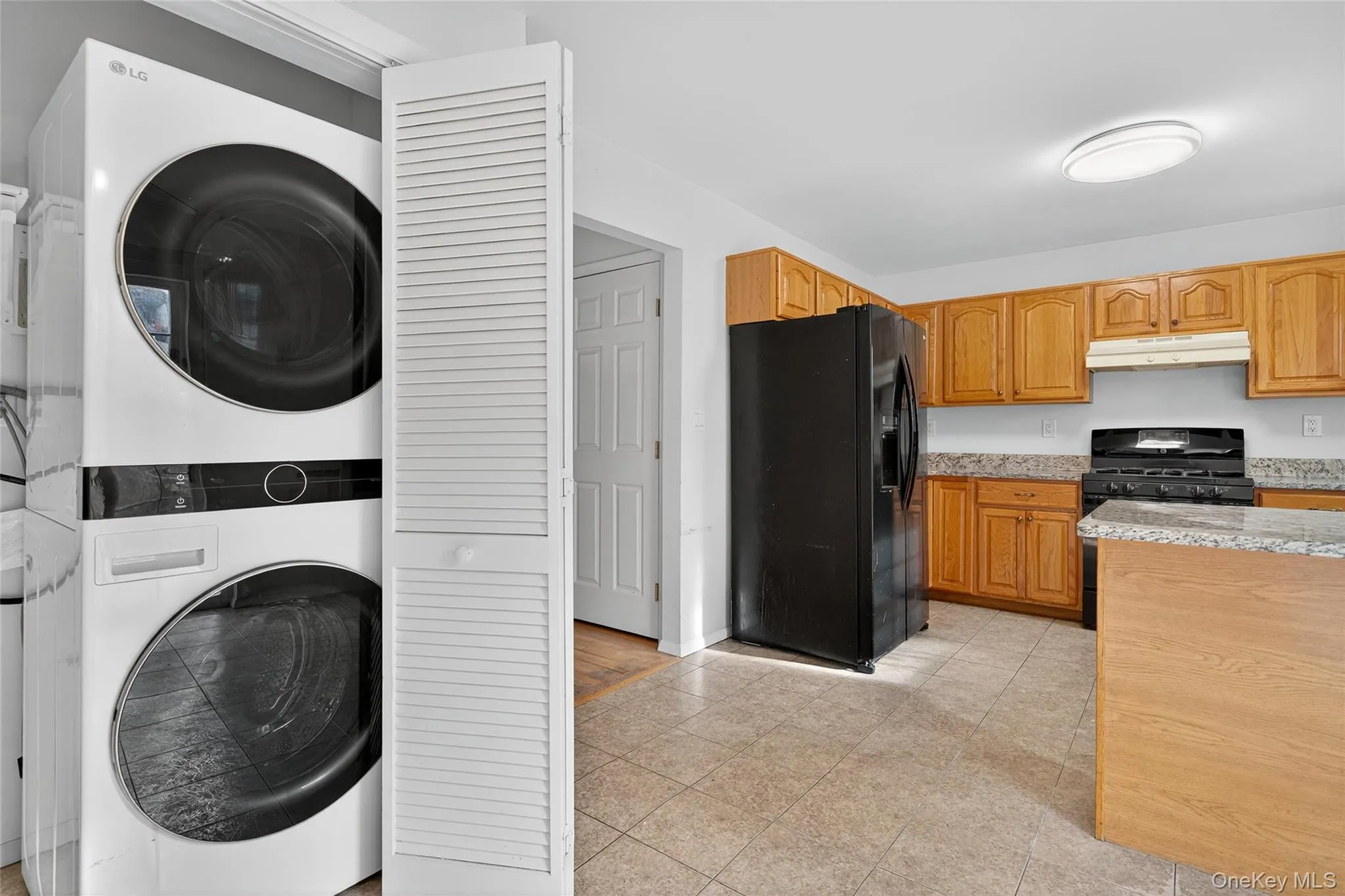 Kitchen featuring black appliances, stacked washer and clothes dryer, light stone counters, and under cabinet range hood Kitchen featuring black appliances, stacked washer and clothes dryer, light stone counters, and under cabinet range hood