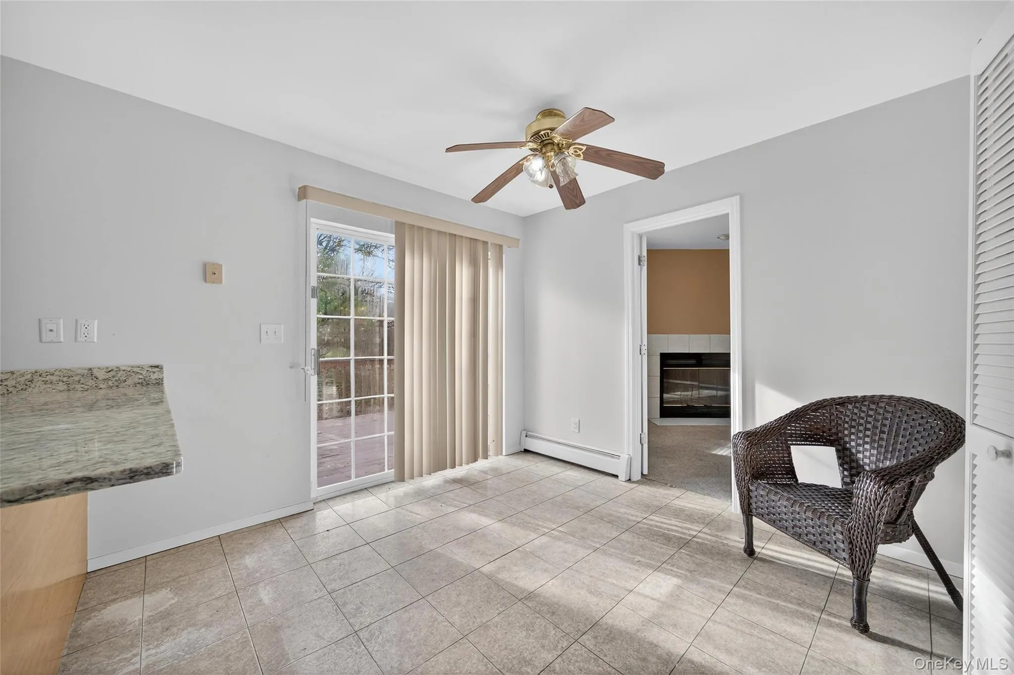 Living area featuring a baseboard heating unit, ceiling fan, a fireplace, and light tile patterned flooring Living area featuring a baseboard heating unit, ceiling fan, a fireplace, and light tile patterned flooring