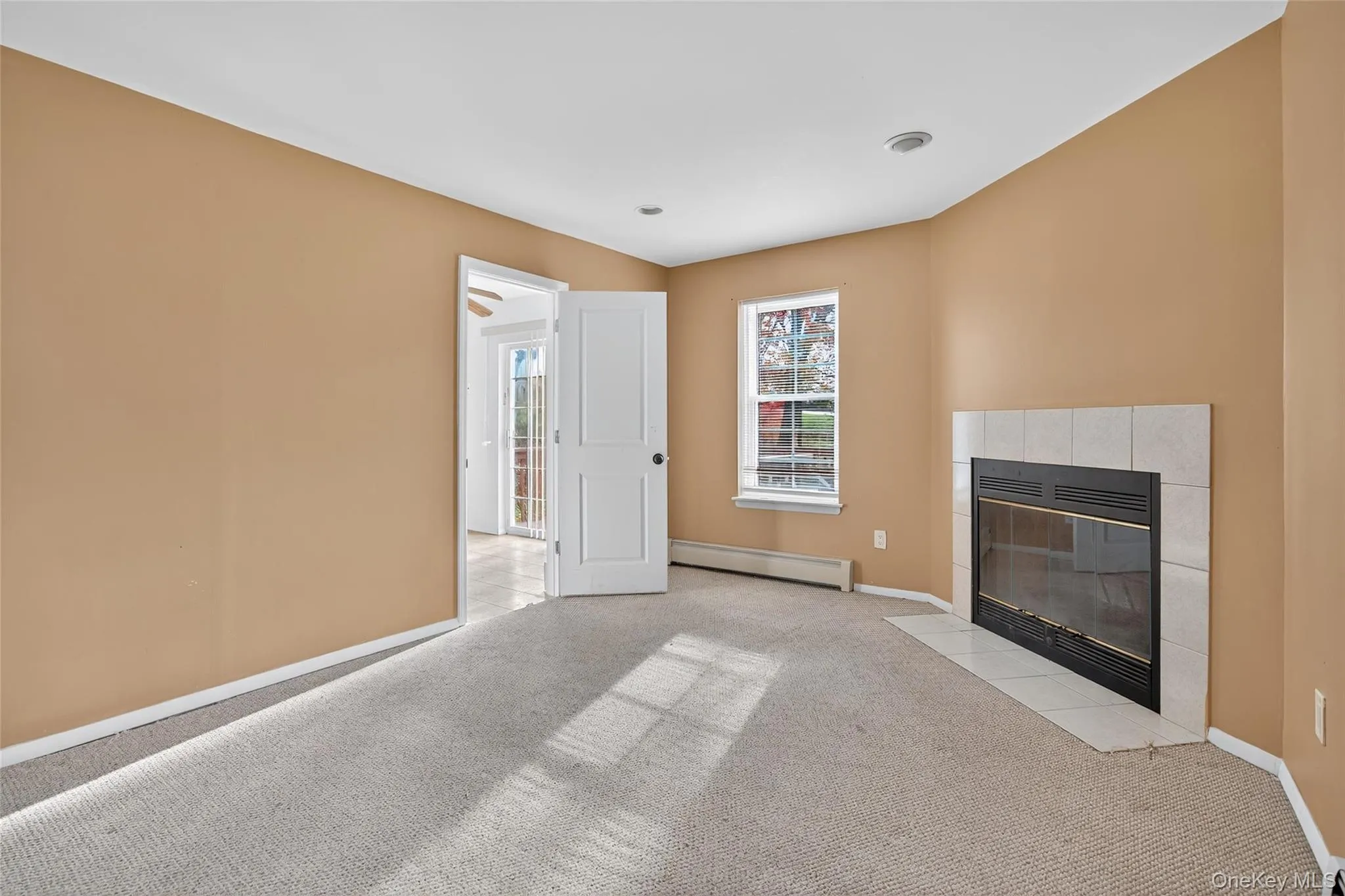 Unfurnished living room with a tile fireplace, carpet flooring, and baseboard heating Unfurnished living room with a tile fireplace, carpet flooring, and baseboard heating