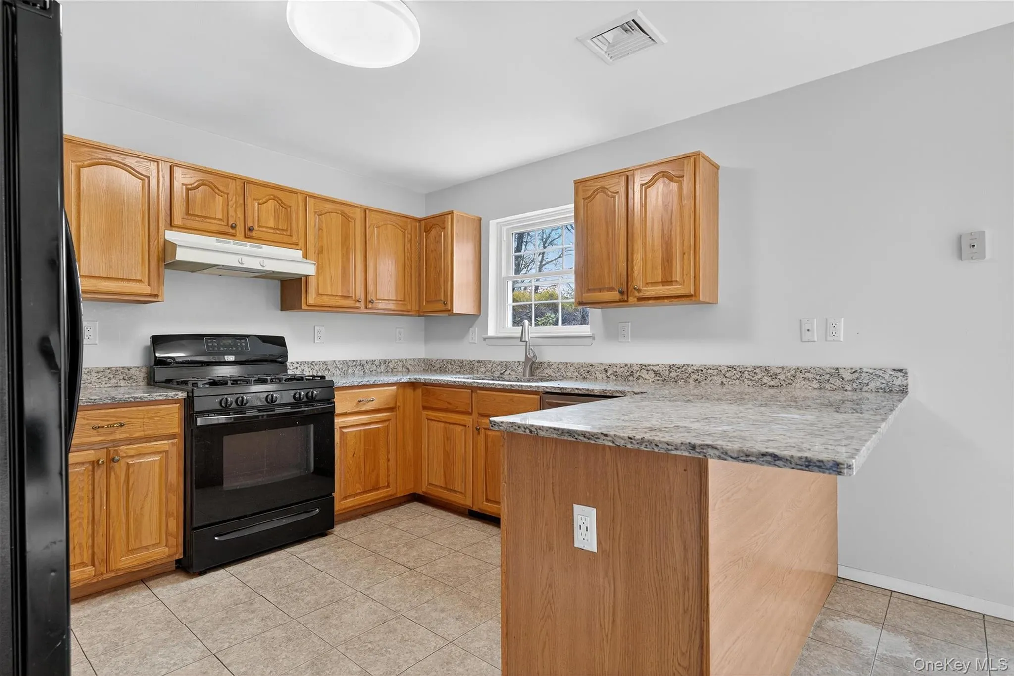 Kitchen featuring black appliances, light stone countertops, light tile patterned floors, under cabinet range hood, and a peninsula Kitchen featuring black appliances, light stone countertops, light tile patterned floors, under cabinet range hood, and a peninsula