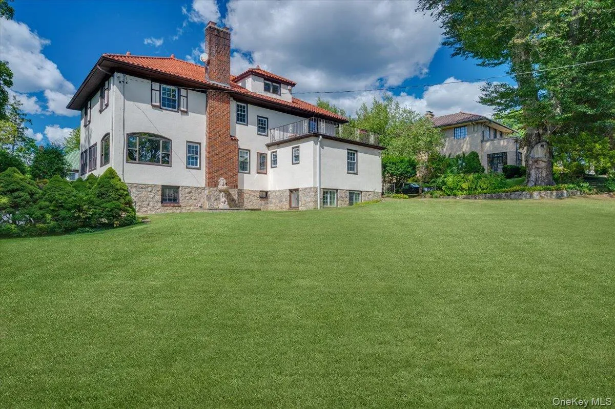 Back of property with stucco siding, a chimney, a lawn, and a tiled roof Back of property with stucco siding, a chimney, a lawn, and a tiled roof