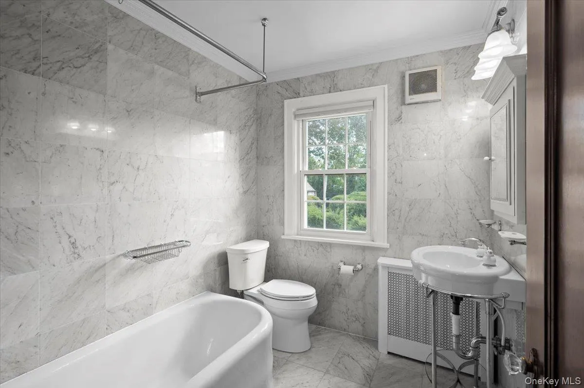 Full bathroom featuring tile walls, ornamental molding, light marble finish floors, and radiator Full bathroom featuring tile walls, ornamental molding, light marble finish floors, and radiator