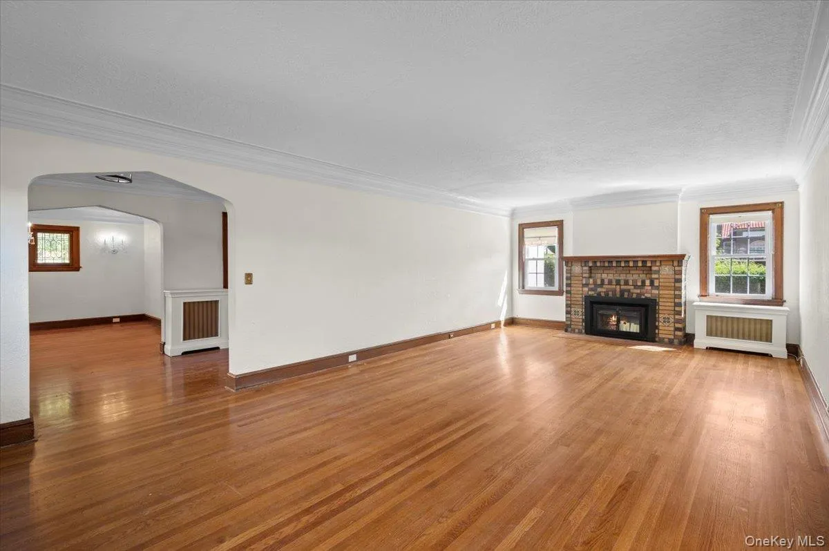 Unfurnished living room with ornamental molding, wood finished floors, radiator heating unit, arched walkways, and a fireplace Unfurnished living room with ornamental molding, wood finished floors, radiator heating unit, arched walkways, and a fireplace