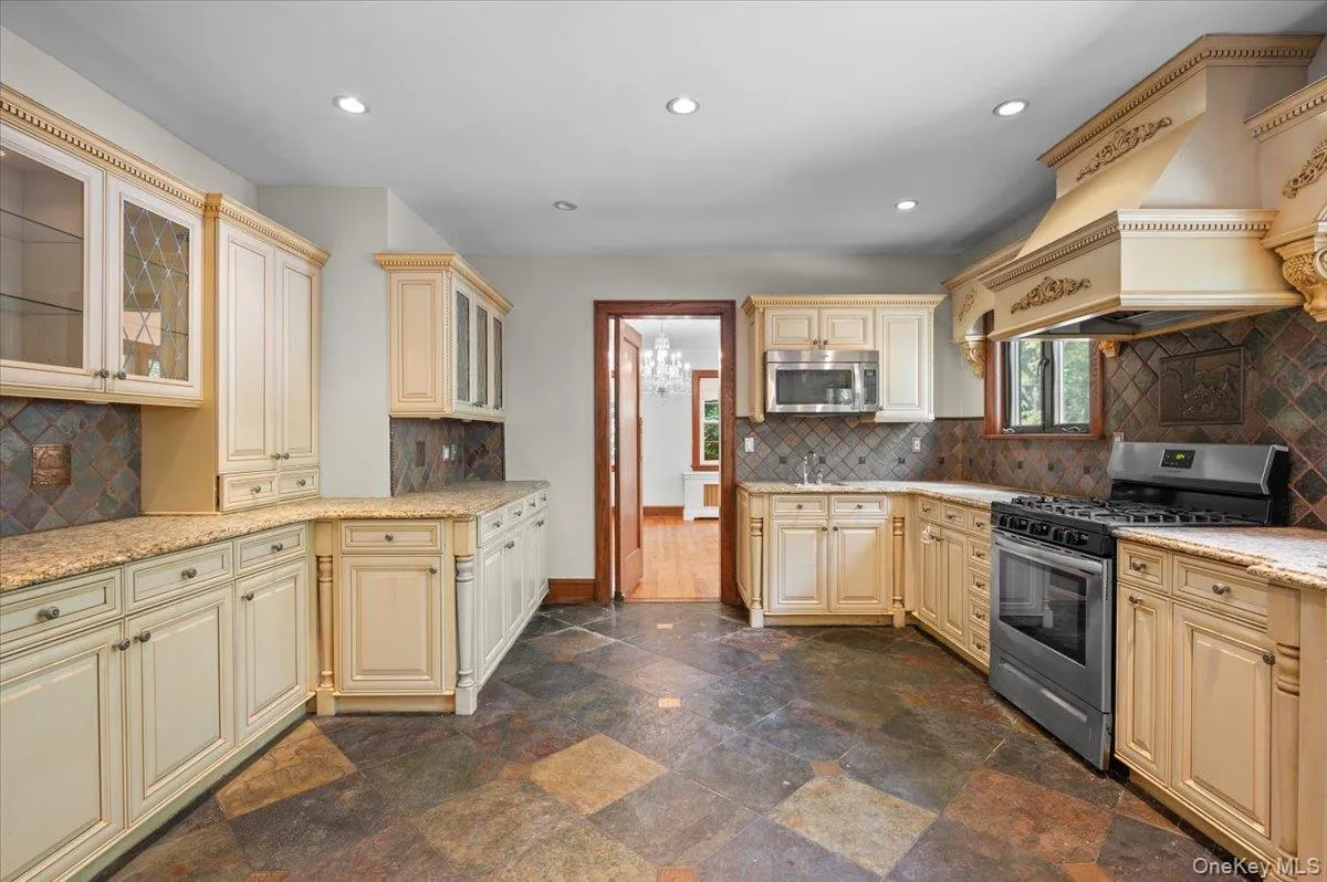Kitchen with tasteful backsplash, cream cabinets, stainless steel appliances, recessed lighting, and custom exhaust hood Kitchen with tasteful backsplash, cream cabinets, stainless steel appliances, recessed lighting, and custom exhaust hood
