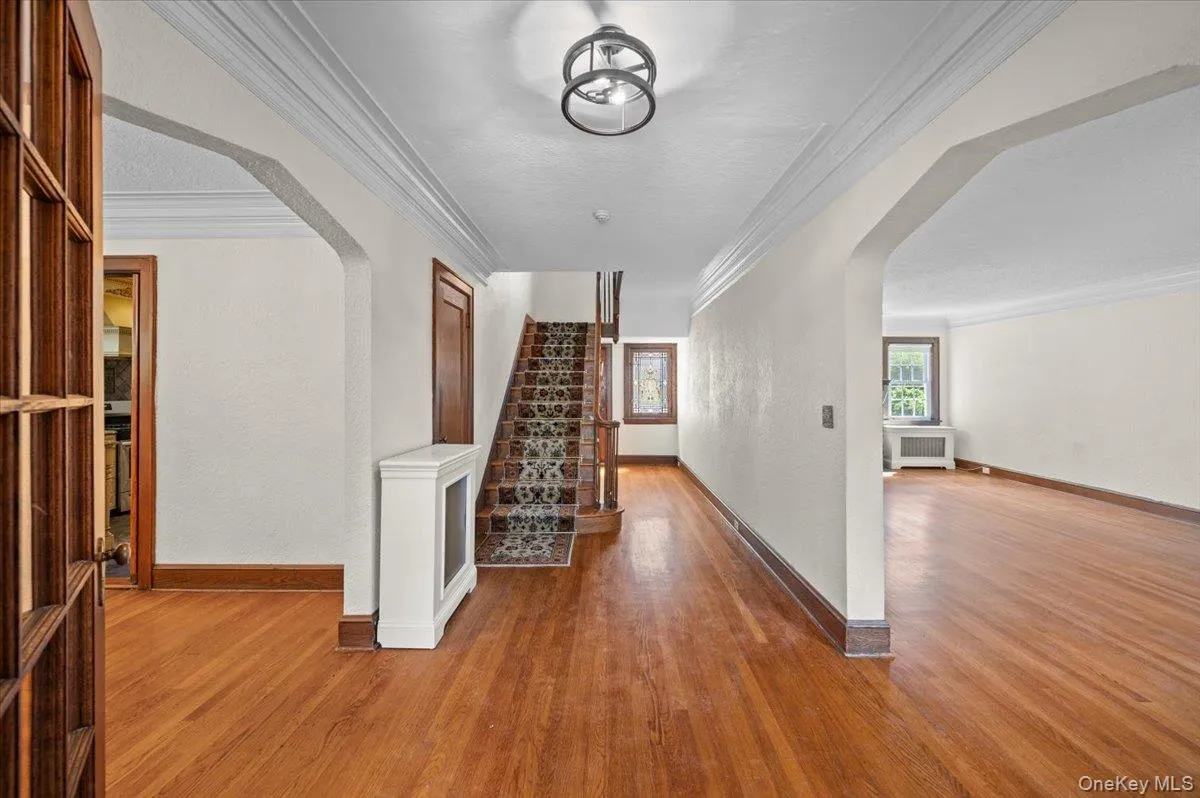 Hallway with arched walkways, crown molding, wood finished floors, radiator heating unit, and a textured ceiling Hallway with arched walkways, crown molding, wood finished floors, radiator heating unit, and a textured ceiling