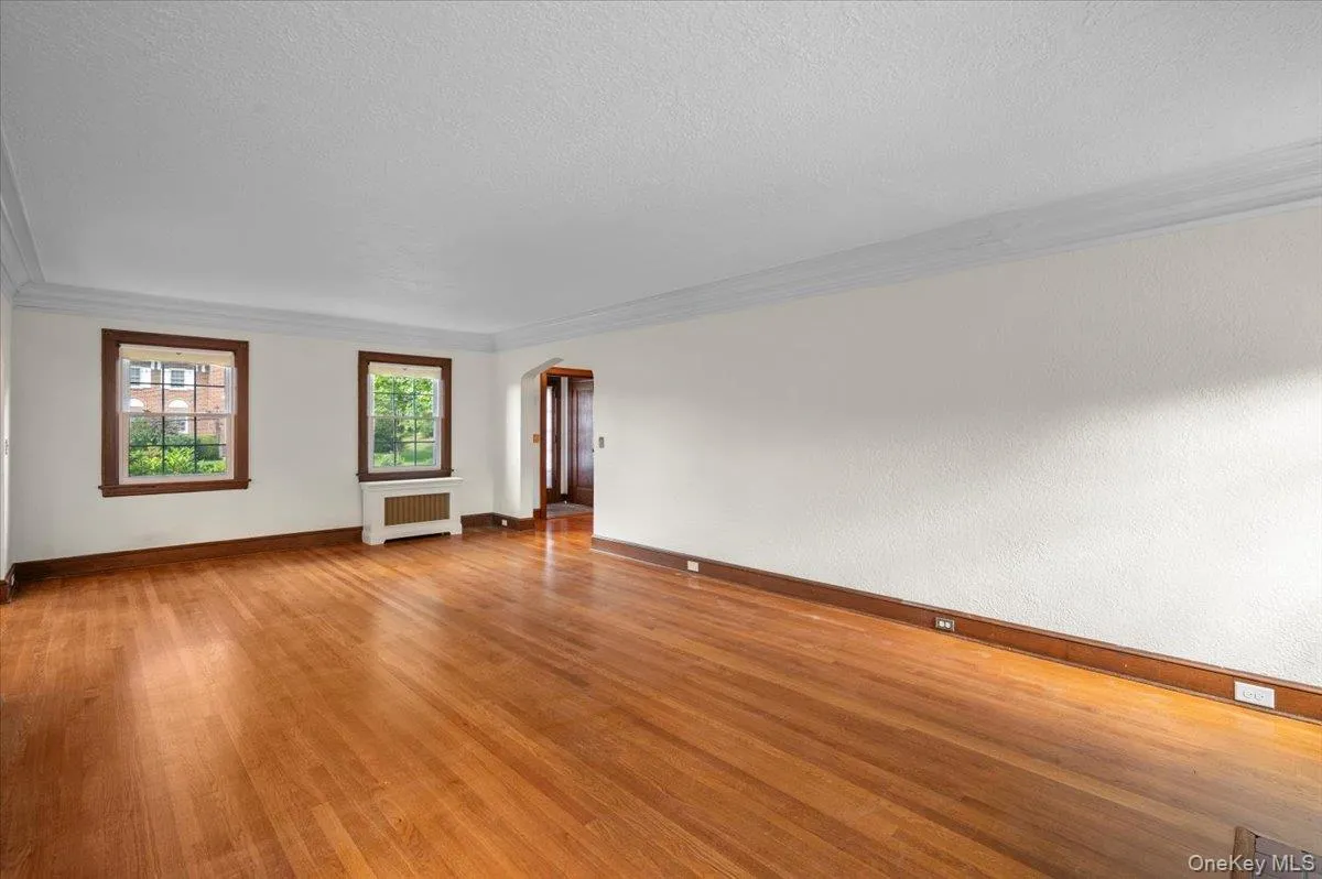 Unfurnished room featuring arched walkways, light wood-style floors, radiator, ornamental molding, and a textured ceiling Unfurnished room featuring arched walkways, light wood-style floors, radiator, ornamental molding, and a textured ceiling