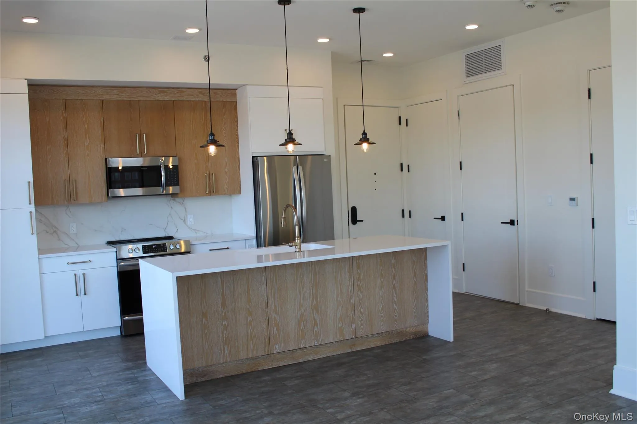 Kitchen with appliances with stainless steel finishes, decorative light fixtures, decorative backsplash, light stone counters, and recessed lighting Kitchen with appliances with stainless steel finishes, decorative light fixtures, decorative backsplash, light stone counters, and recessed lighting