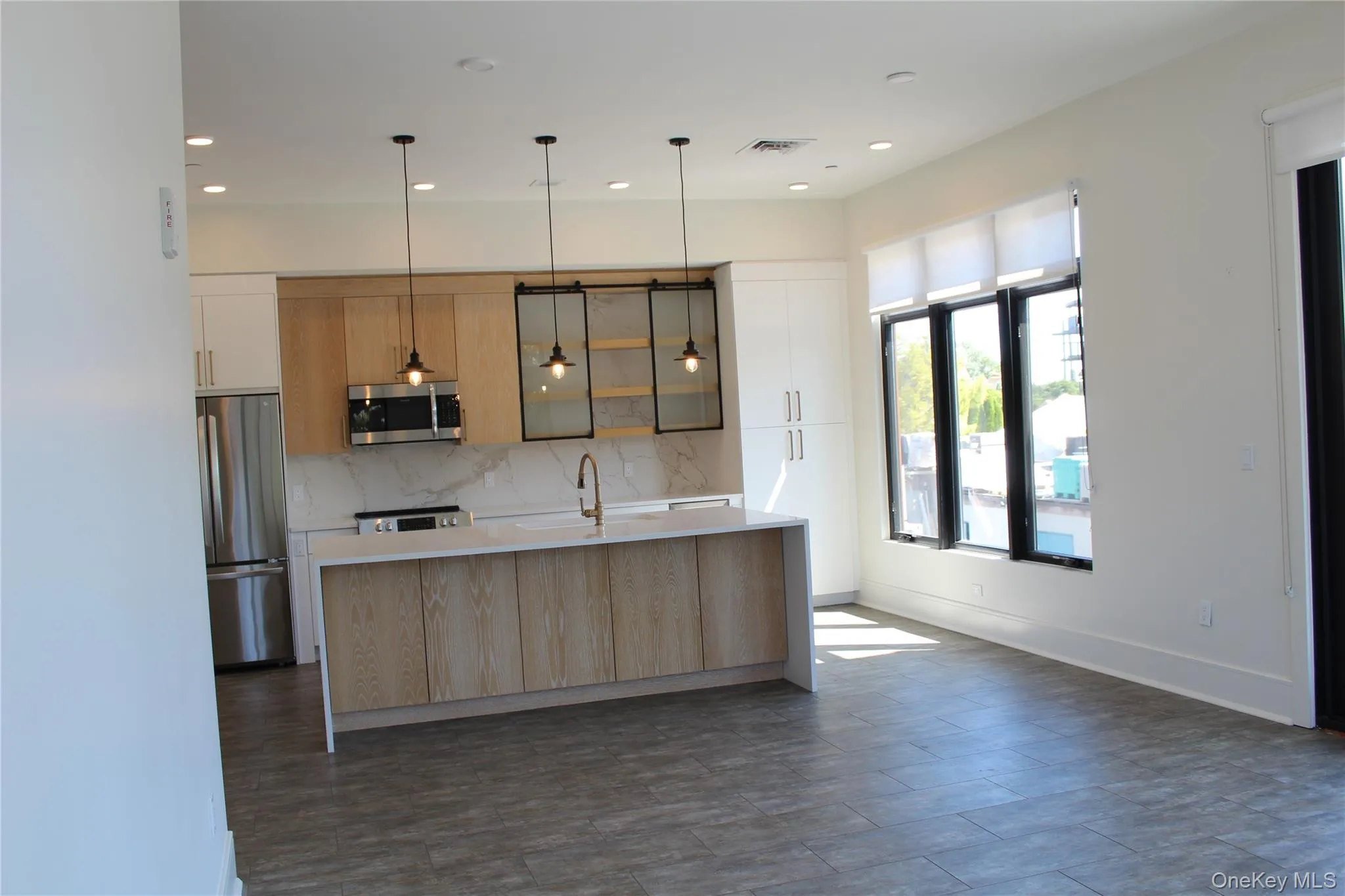 Kitchen with modern cabinets, hanging light fixtures, backsplash, appliances with stainless steel finishes, and light brown cabinetry Kitchen with modern cabinets, hanging light fixtures, backsplash, appliances with stainless steel finishes, and light brown cabinetry