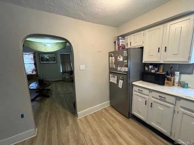 Kitchen featuring light countertops, arched walkways, light wood finished floors, white cabinets, and a textured ceiling Kitchen featuring light countertops, arched walkways, light wood finished floors, white cabinets, and a textured ceiling