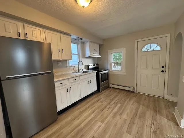 Kitchen with stainless steel appliances, light countertops, a textured ceiling, light wood-type flooring, and white cabinets Kitchen with stainless steel appliances, light countertops, a textured ceiling, light wood-type flooring, and white cabinets
