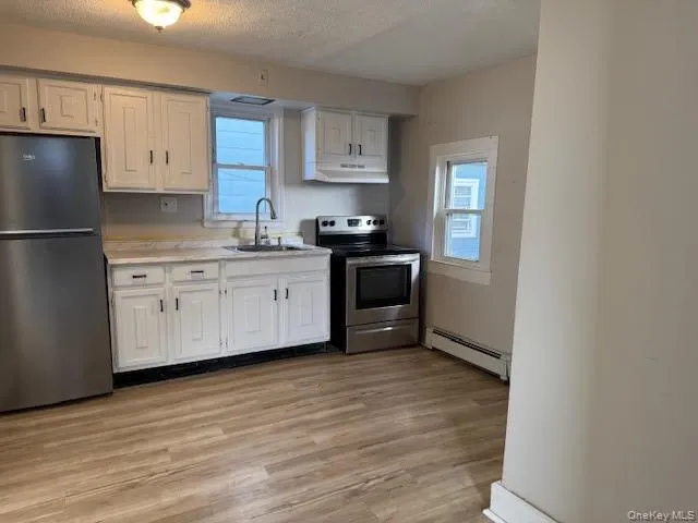 Kitchen with appliances with stainless steel finishes, light wood-type flooring, white cabinetry, light countertops, and a textured ceiling Kitchen with appliances with stainless steel finishes, light wood-type flooring, white cabinetry, light countertops, and a textured ceiling