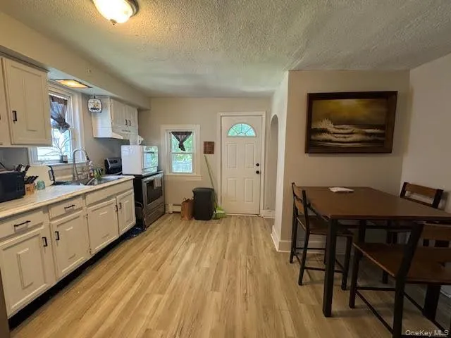Kitchen featuring a textured ceiling, light countertops, electric stove, light wood-style flooring, and white cabinetry Kitchen featuring a textured ceiling, light countertops, electric stove, light wood-style flooring, and white cabinetry