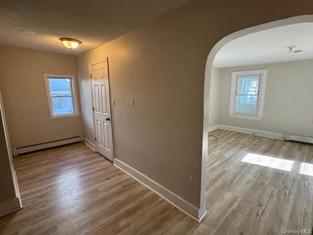 Hallway featuring light wood-style flooring, a baseboard heating unit, arched walkways, and a textured ceiling Hallway featuring light wood-style flooring, a baseboard heating unit, arched walkways, and a textured ceiling