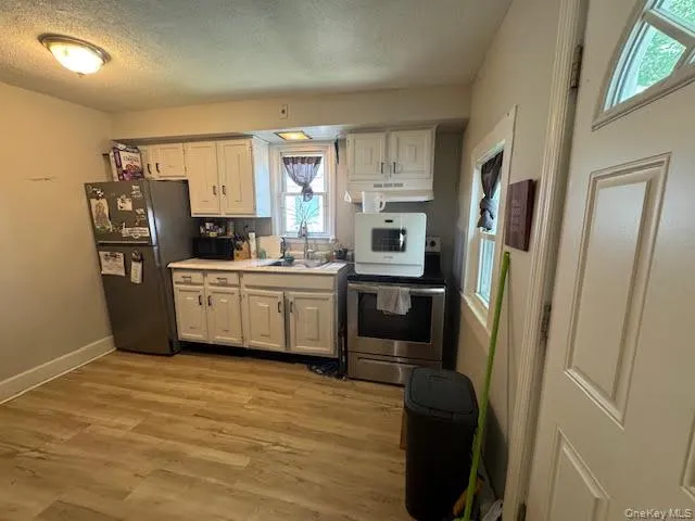 Kitchen with black appliances, light countertops, light wood-style floors, a textured ceiling, and white cabinetry Kitchen with black appliances, light countertops, light wood-style floors, a textured ceiling, and white cabinetry