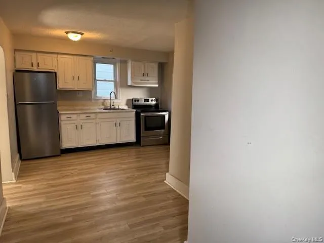 Kitchen with stainless steel appliances, light countertops, dark wood finished floors, and white cabinetry Kitchen with stainless steel appliances, light countertops, dark wood finished floors, and white cabinetry