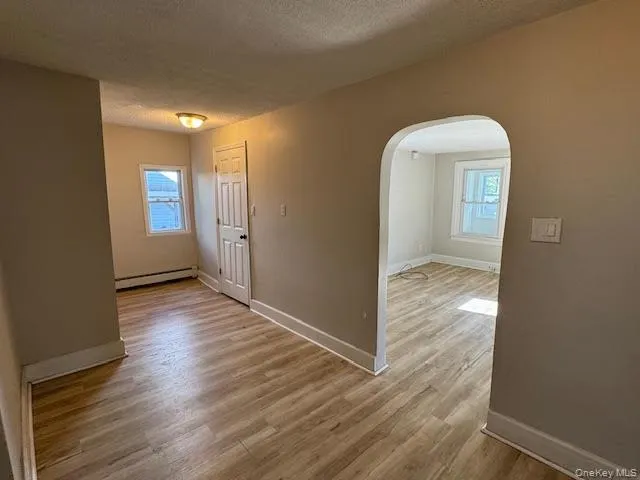 Spare room with arched walkways, light wood-type flooring, a textured ceiling, and a baseboard radiator Spare room with arched walkways, light wood-type flooring, a textured ceiling, and a baseboard radiator