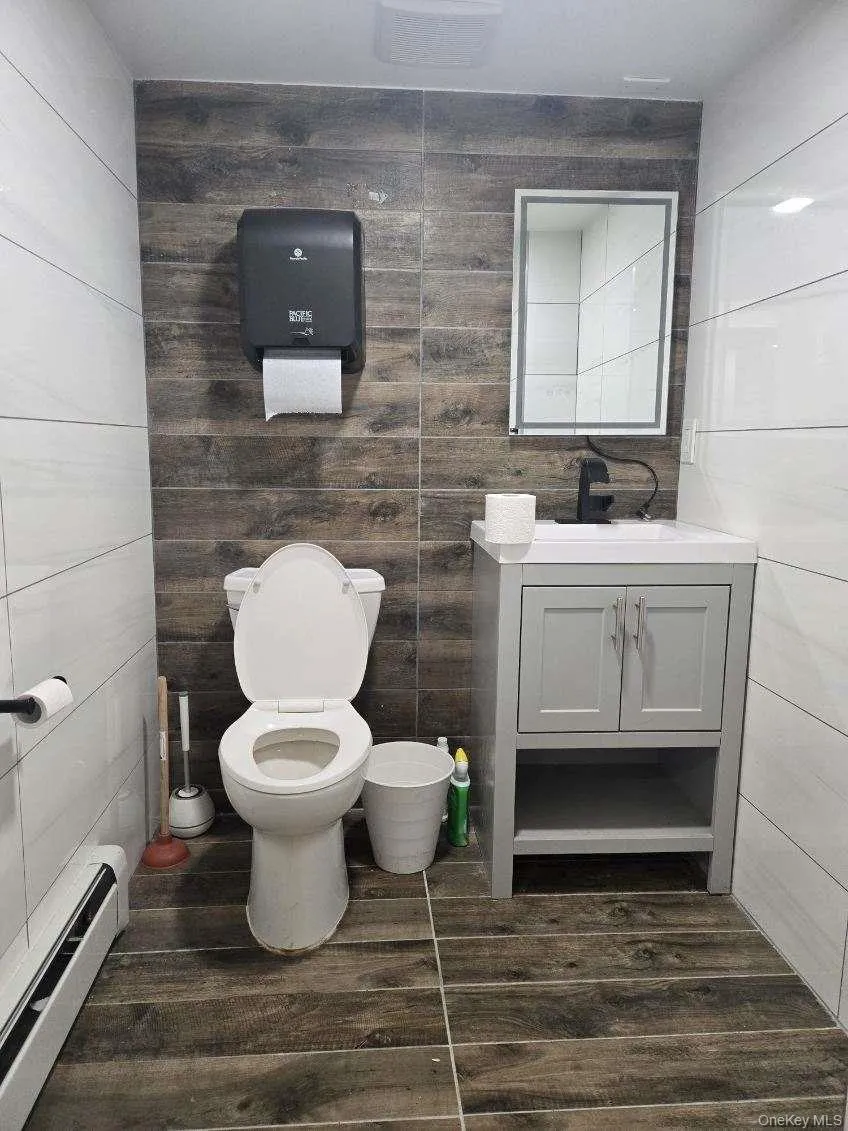 Bathroom with a baseboard heating unit, tile walls, vanity, and dark wood-style floors Bathroom with a baseboard heating unit, tile walls, vanity, and dark wood-style floors