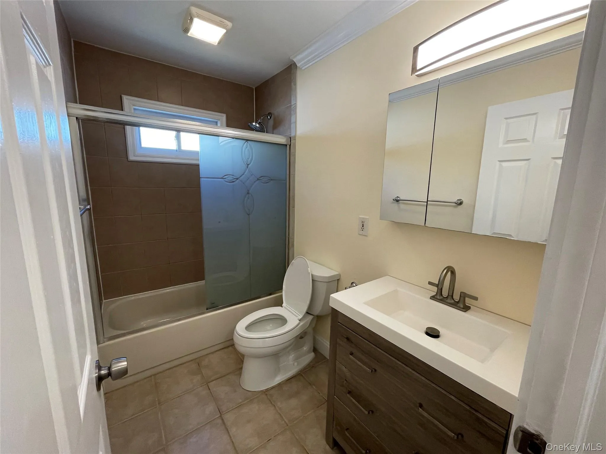 Bathroom featuring combined bath / shower with glass door, vanity, light tile patterned floors, and crown molding Bathroom featuring combined bath / shower with glass door, vanity, light tile patterned floors, and crown molding