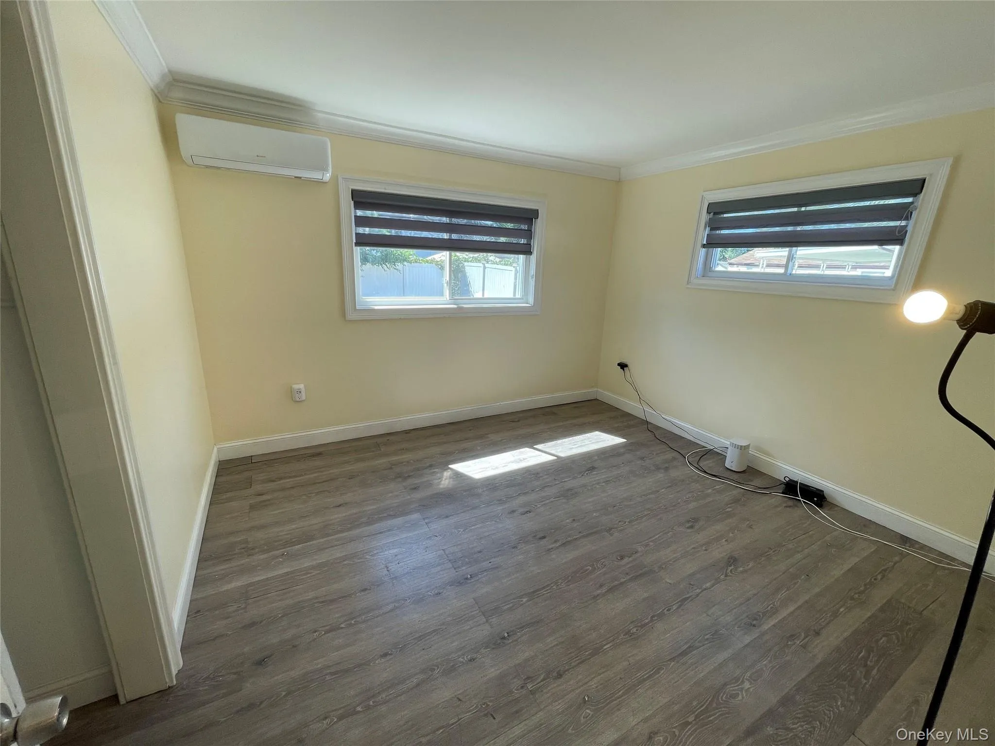 Empty room with crown molding, wood finished floors, and a wall mounted AC Empty room with crown molding, wood finished floors, and a wall mounted AC