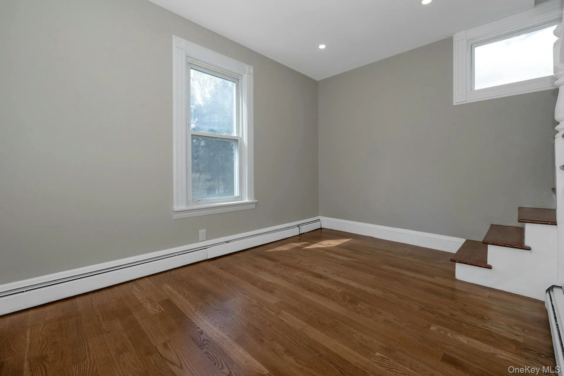 Empty room featuring a baseboard radiator, dark wood finished floors, recessed lighting, and stairs Empty room featuring a baseboard radiator, dark wood finished floors, recessed lighting, and stairs