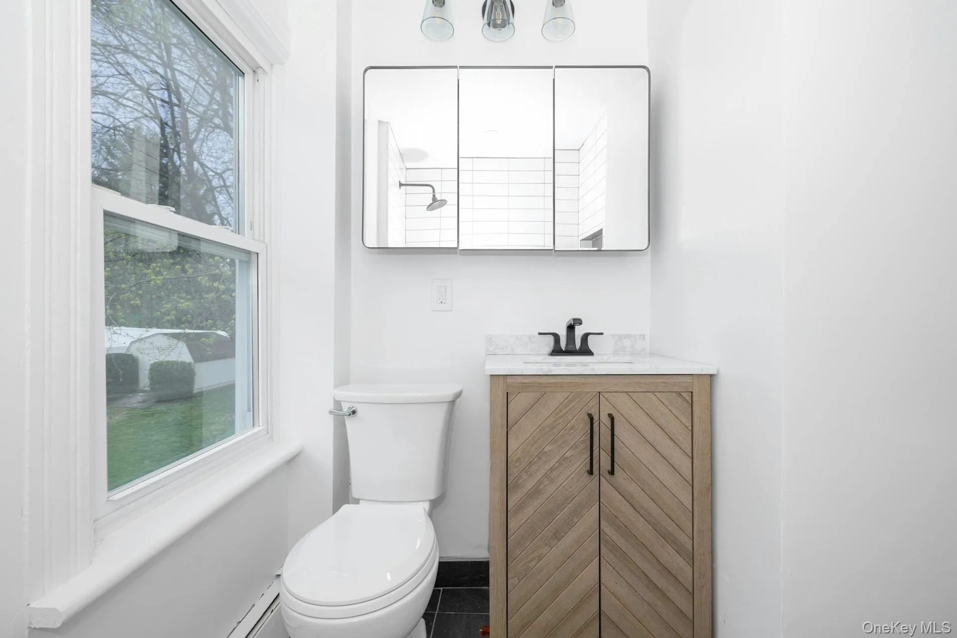 Half bath featuring vanity, baseboard heating, and dark tile patterned floors Half bath featuring vanity, baseboard heating, and dark tile patterned floors