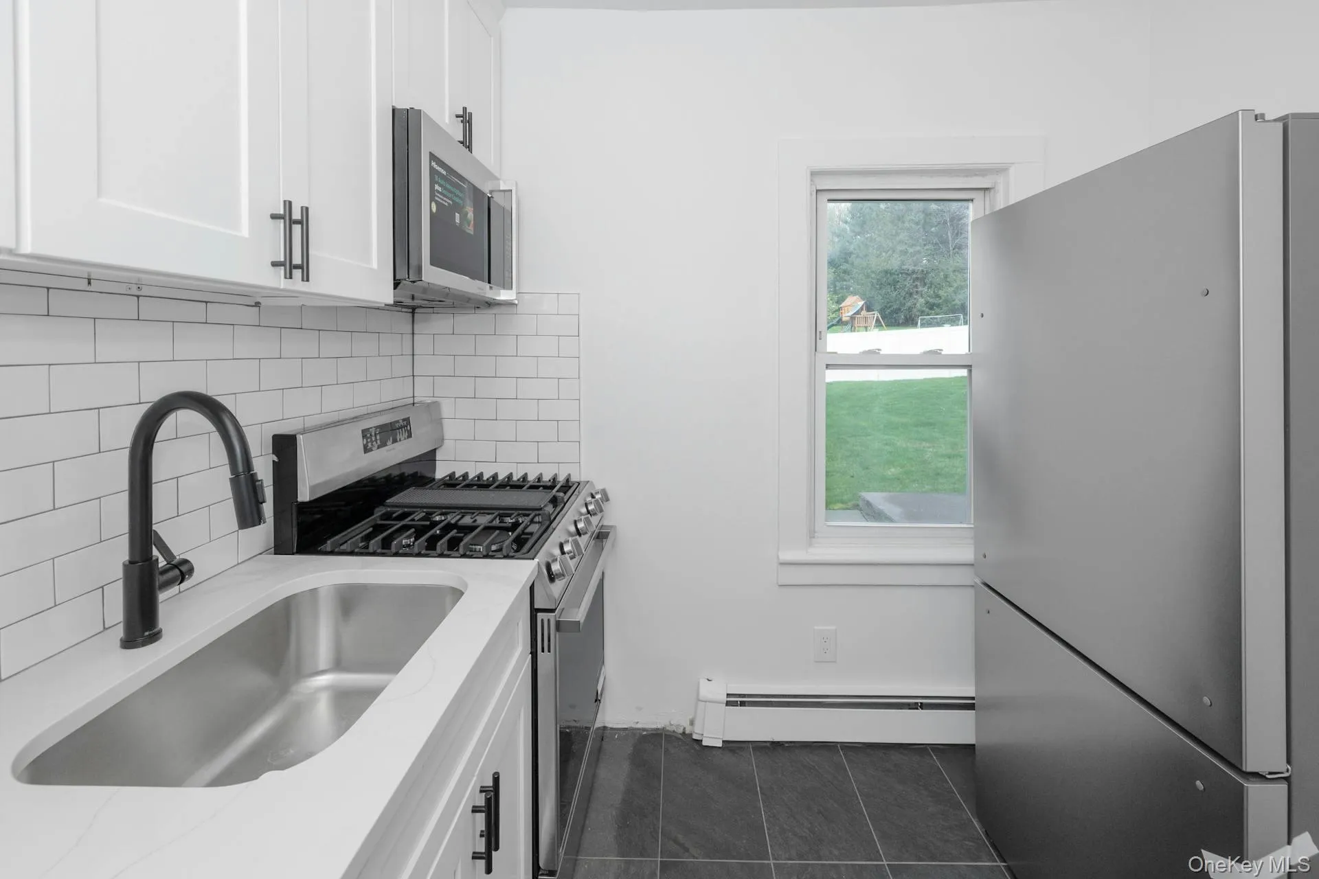 Kitchen featuring appliances with stainless steel finishes, white cabinetry, tasteful backsplash, a baseboard heating unit, and light stone countertops Kitchen featuring appliances with stainless steel finishes, white cabinetry, tasteful backsplash, a baseboard heating unit, and light stone countertops