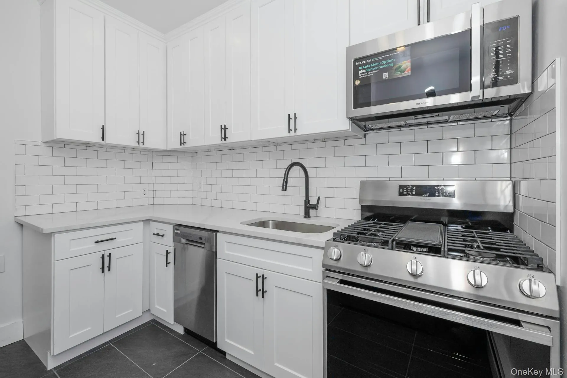 Kitchen featuring stainless steel appliances, light stone countertops, decorative backsplash, dark tile patterned flooring, and white cabinetry Kitchen featuring stainless steel appliances, light stone countertops, decorative backsplash, dark tile patterned flooring, and white cabinetry